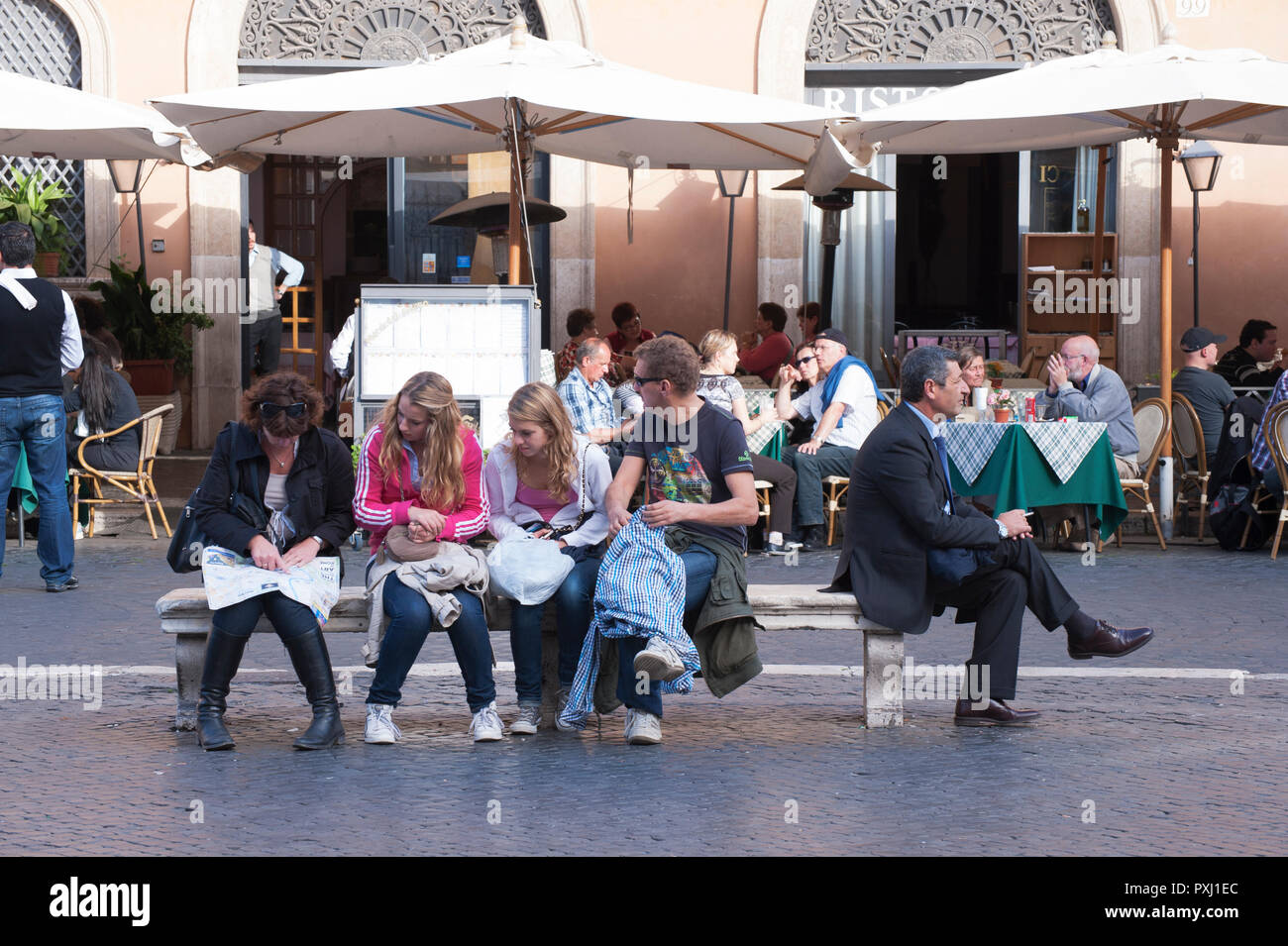 Sitting on the same bench, tourists consulting a map and lone elegant man smoking a cigarette, Piazza Navona, Rome. Stock Photo
