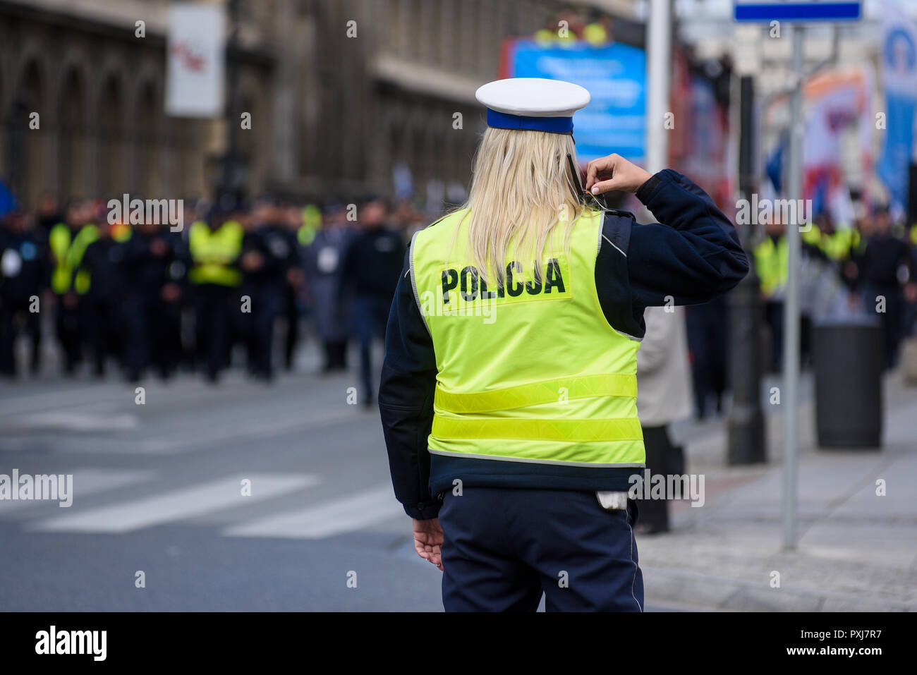 Police woman standing on the cross road and controlling the traffic. Dressed in a police uniform with yellow west. Stock Photo