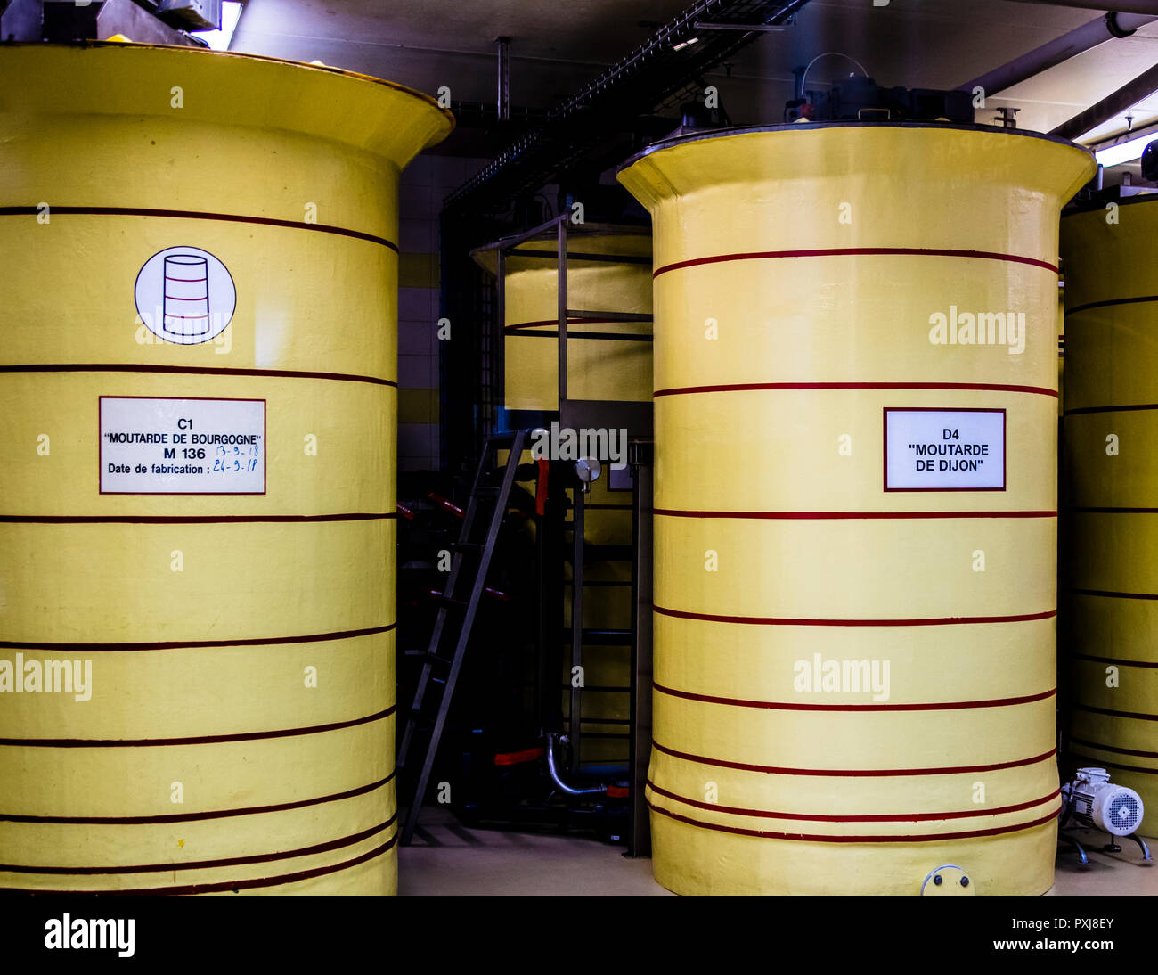 Yellow storage tanks labelled "Moutarde de Bourgogne" and "Moutarde de Dijon" stand side by side in the production hall of Edmond Fallot in Beaune in Burgundy, France. The finished mustard rests here for 24 hours before it is bottled. Stock Photo