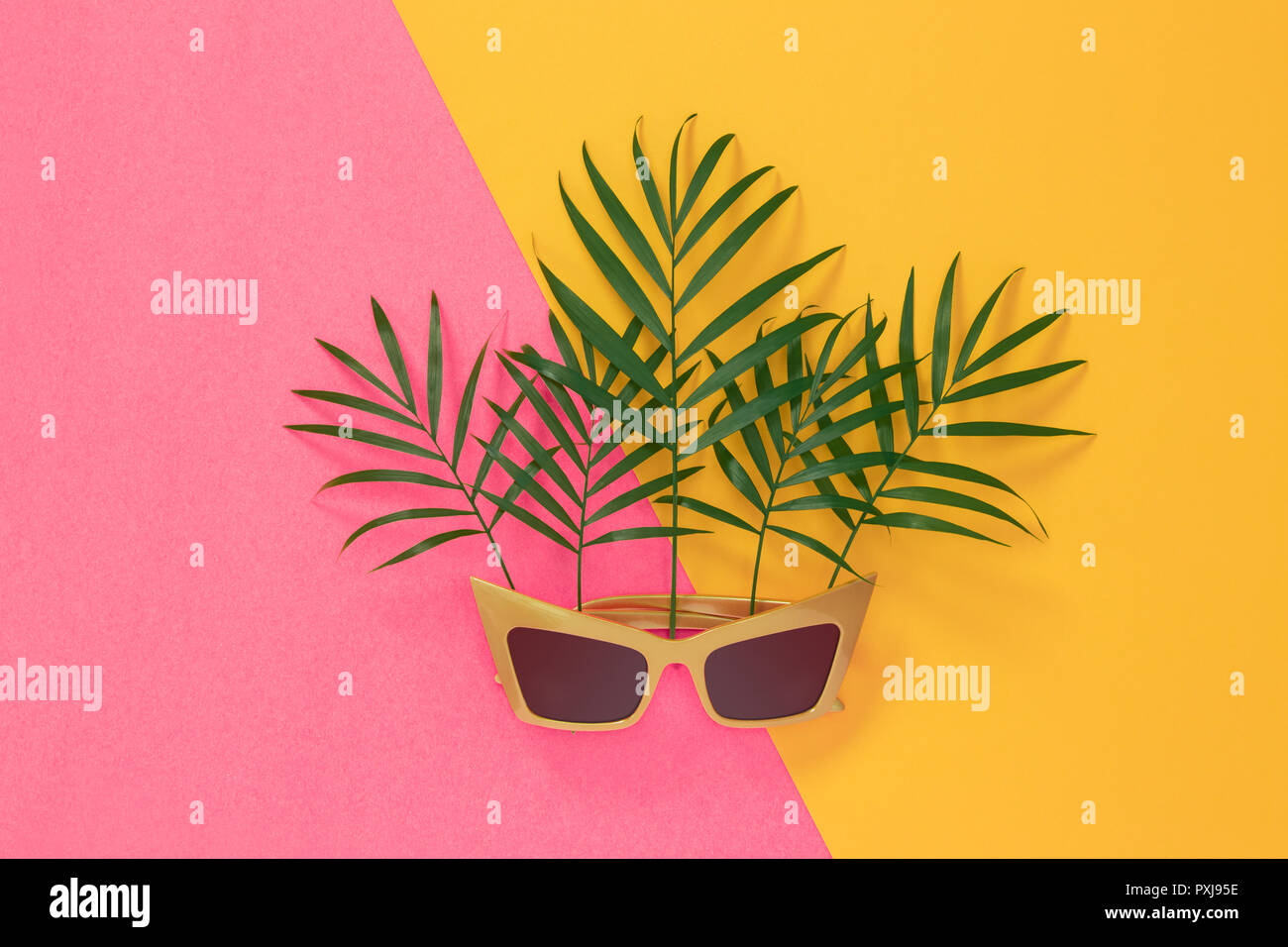 Palm leaves and sunglasses on vibrant pink and yellow background ...