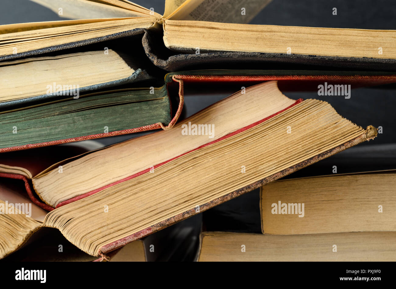 Close up of a pile of old text books, opened as if study in progress, stacked untidily with blackboard background. Stock Photo
