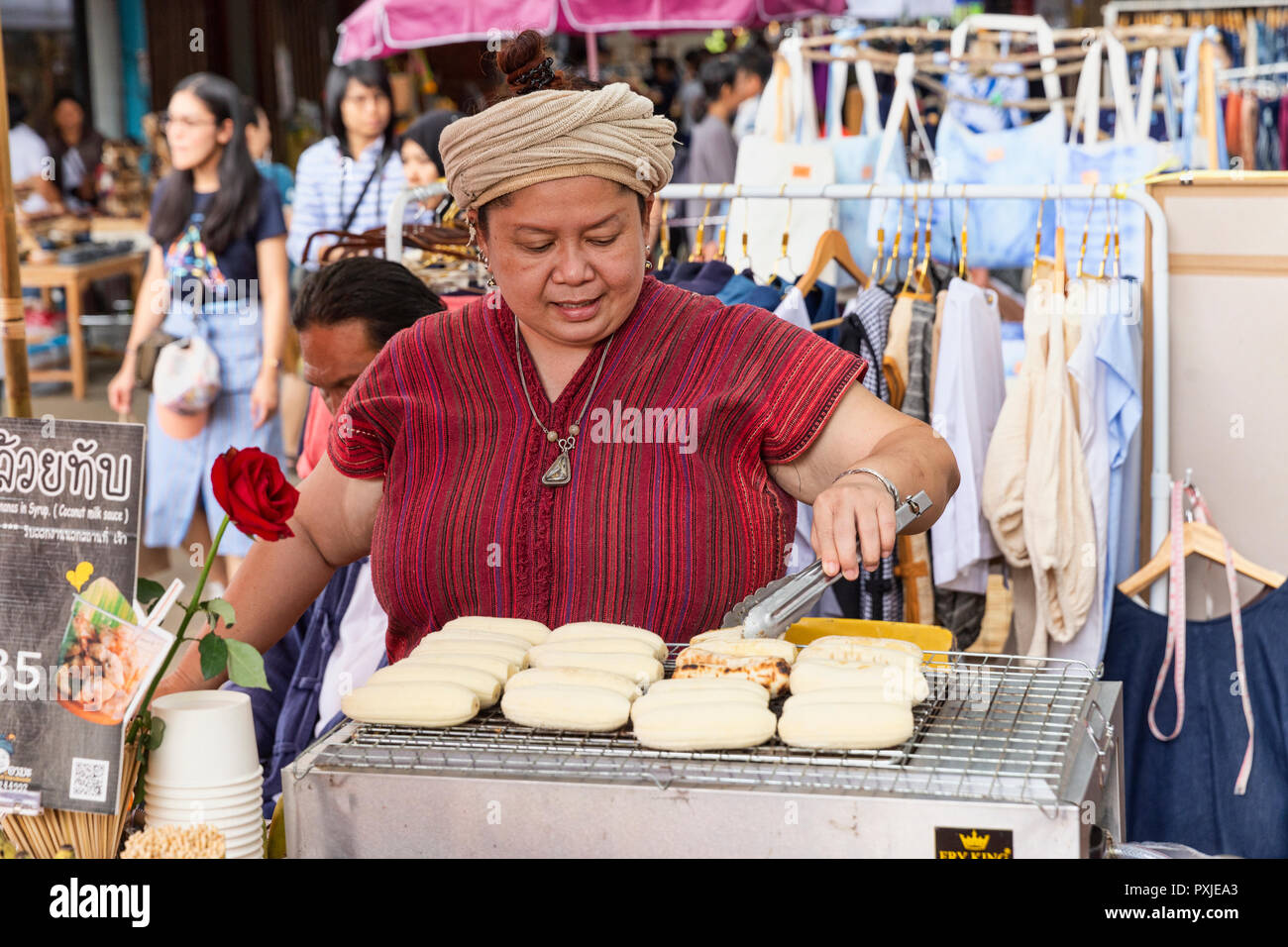 Thai street vendor in traditional northern clothes grilling bananas at JingJai Farmer's Market, Chiang Mai, Thailand Stock Photo