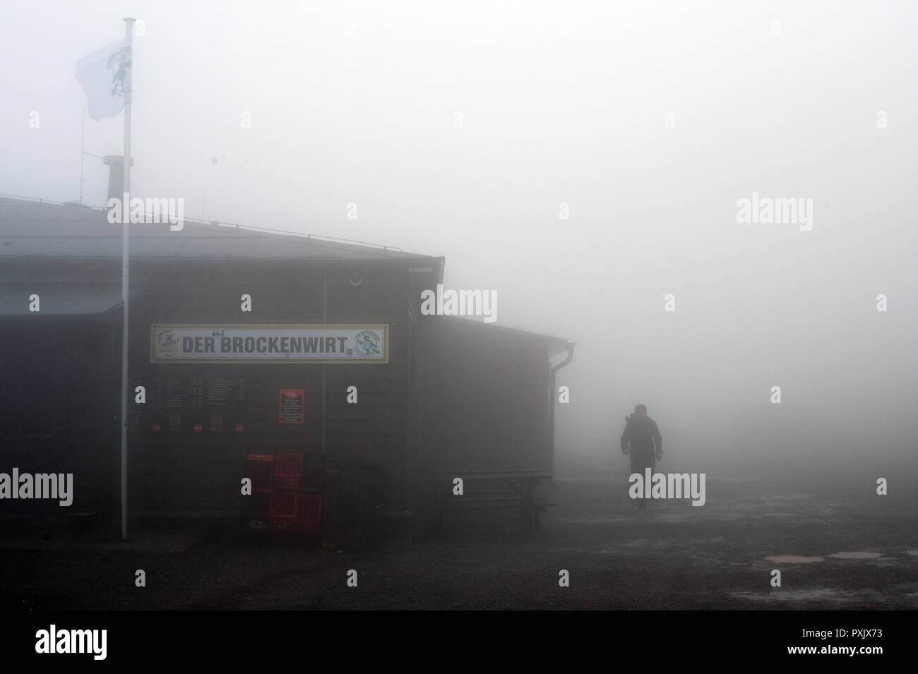 23 October 2018, Saxony-Anhalt, Brockengipfel: A hiker walks past the Brockenwirt in rain and fog.  The German Weather Service (DWD) has issued a thunderstorm warning for the Harz Mountains. The Harzer Schmalspurbahnen (HSB) have stopped the train service to the summit of the Brocken and are now only running to Drei Annen Hohne station. Photo: Klaus-Dietmar Gabbert/dpa-Zentralbild/dpa Stock Photo