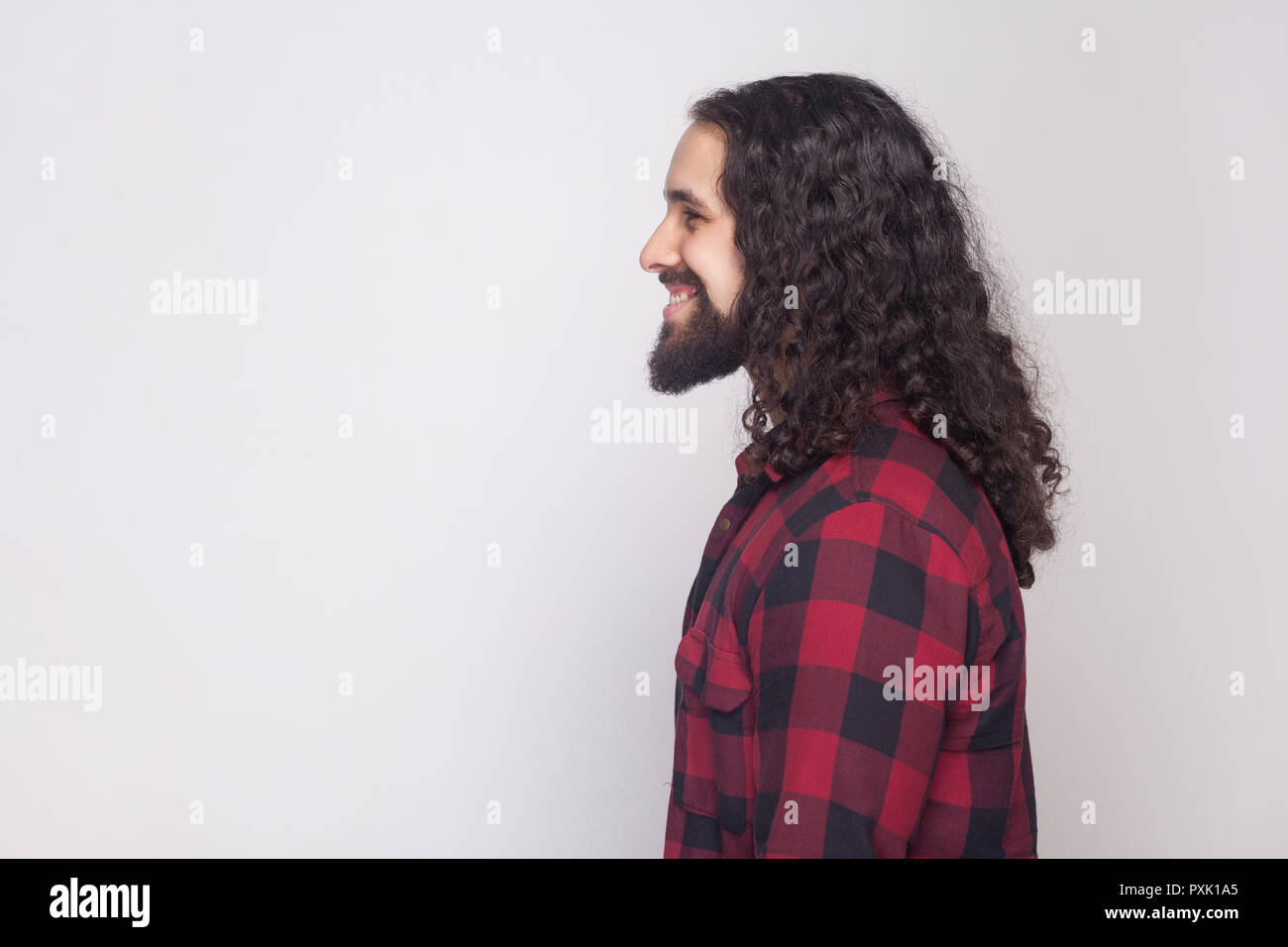 Profile side view portrait of handsome happy man with beard and black long  curly hair in casual style, checkered red shirt standing with toothy smile  Stock Photo - Alamy