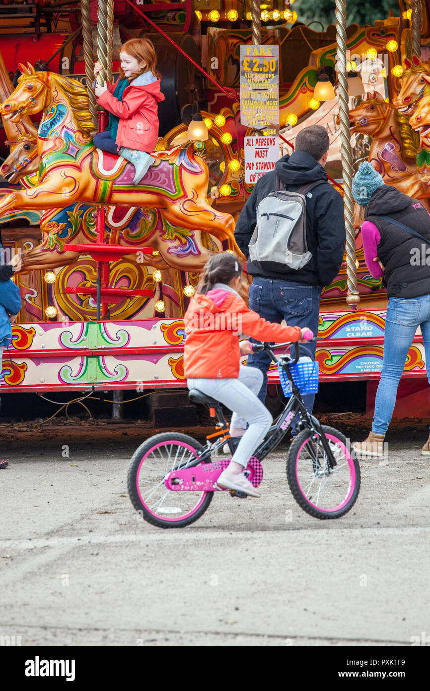 Young girl riding a bike cycle past the hobby horse carousal roundabout