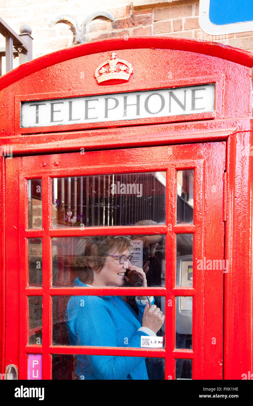 Woman chatting talking using a telephone in an traditional red English telephone box kiosk design  no 6  / K6 designed in 1935 by Sir Gilbert Scott Stock Photo