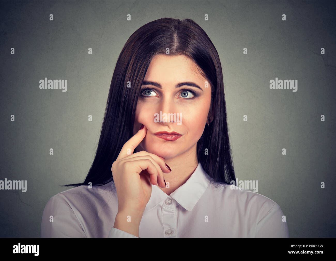 Beautiful young woman in white shirt touching chin in contemplation looking away and thinking Stock Photo