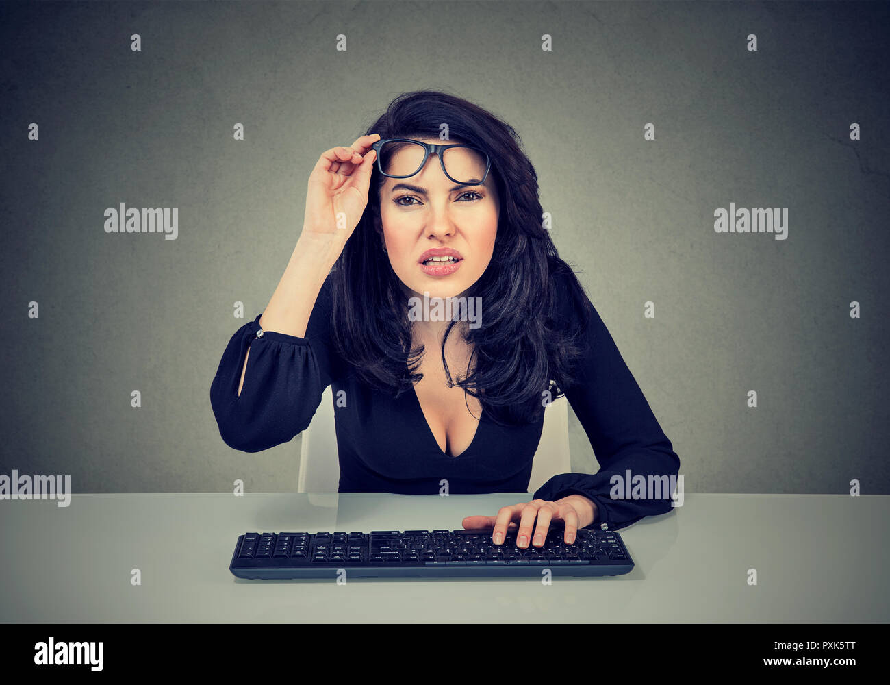 Young business woman using keyboard and squinting eyes having vision problems on gray background Stock Photo