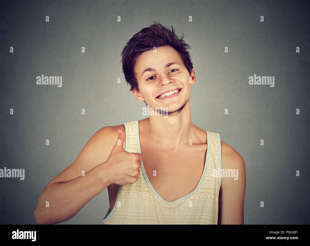 Cheerful teenager man in tank top holding thumb up smiling at camera on gray background Stock Photo