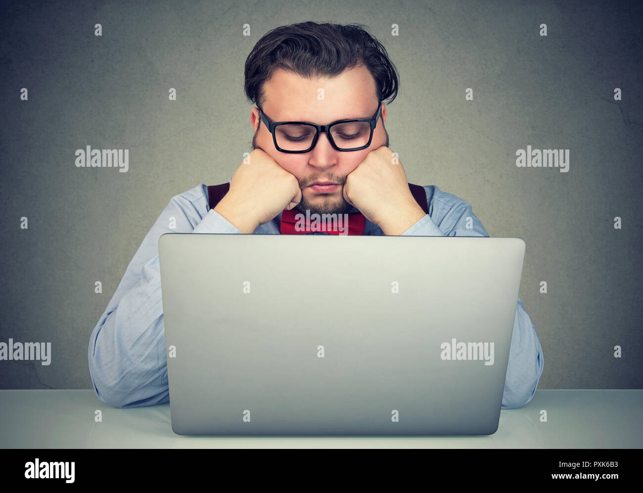 Young obese man sitting at workplace and procrastinating being lazy and distracted. Stock Photo