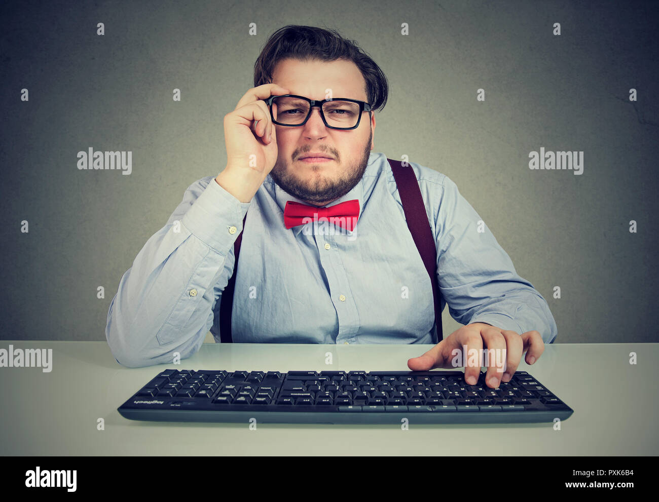 Adult chunky man using keyboard and squinting eyes having vision problems on gray background Stock Photo