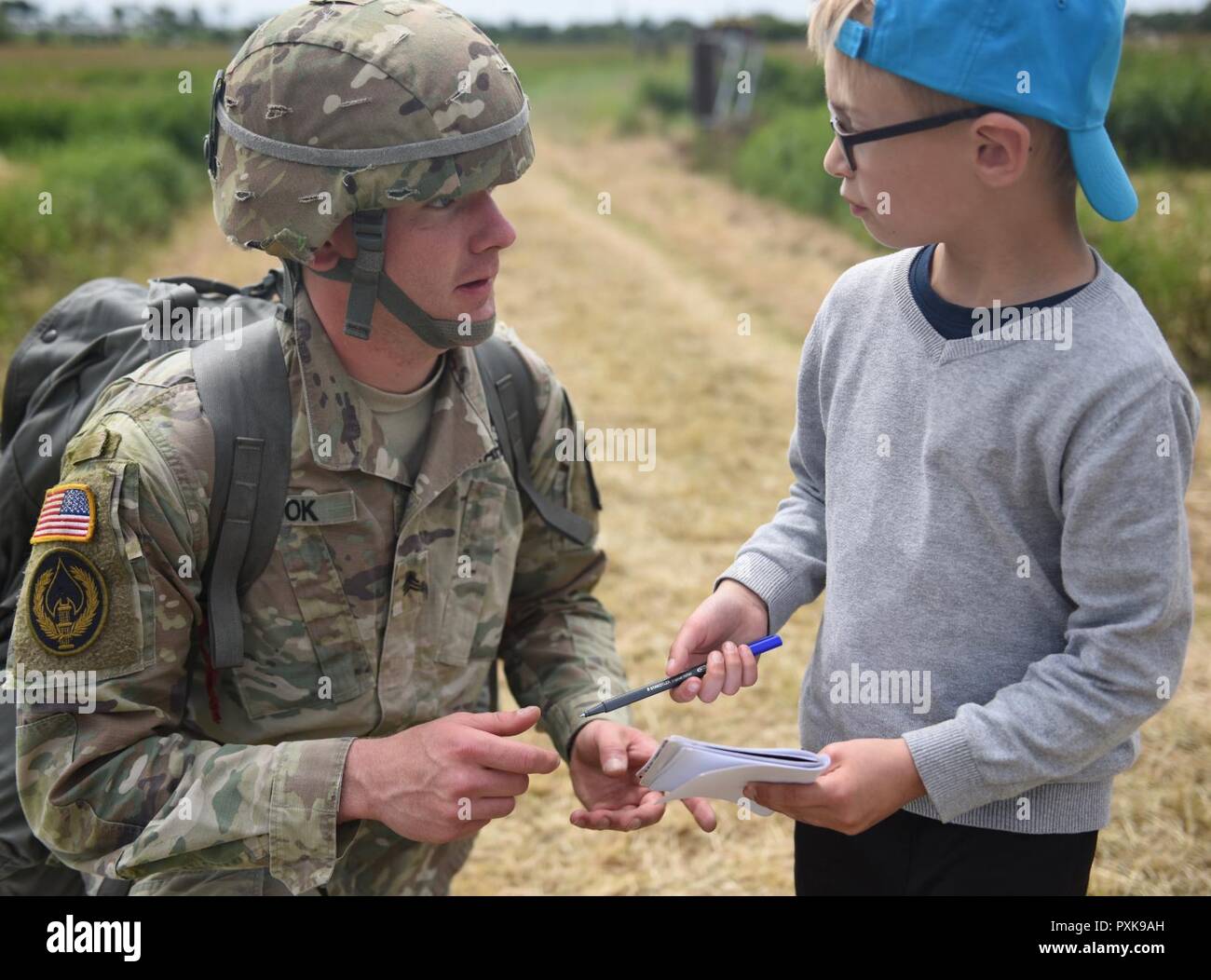 A U.S. Army Paratrooper from the 173rd Airborne Brigade signs an autograph book for a young French boy following the commemorative airborne operation on Iron Mike Drop Zone II in Normandy, France. Paratroopers from across the armed forces and NATO jumped into Normandy to commemorate the 73rd anniversary of Operation Overlord, also known as D-Day. The 173rd Airborne Brigade (Sky Soldiers) is the U.S. Army's Contingency Response Force in Europe, providing rapid forces to the United States European, Africa and Central Commands areas of responsibilities. Forward-based in Italy and Germany along wi Stock Photo