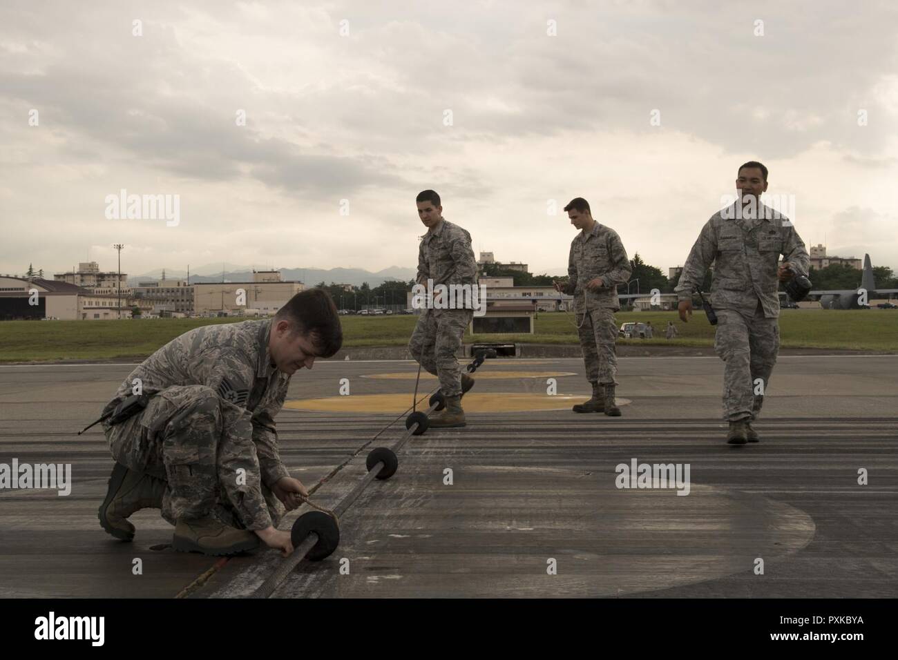 Airmen with the 374th Civil Engineer Squadron power productions shop inspect an emergency aircraft landing cable on the runway at Yokota Air Base, Japan, June 1, 2017, during an annual certification test of Aircraft Arresting System. Testing the system on an annual basis is the responsibility of the 374 CES and 374th Operations Support Squadron airfield management. Stock Photo