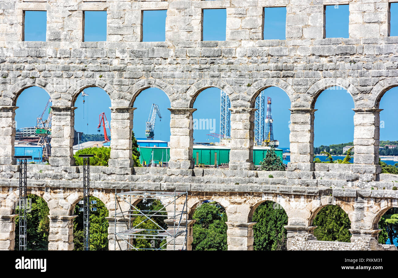 Pula Arena and cranes in a cargo port, Istria, Croatia. Travel destination. Ancient architecture. Stock Photo