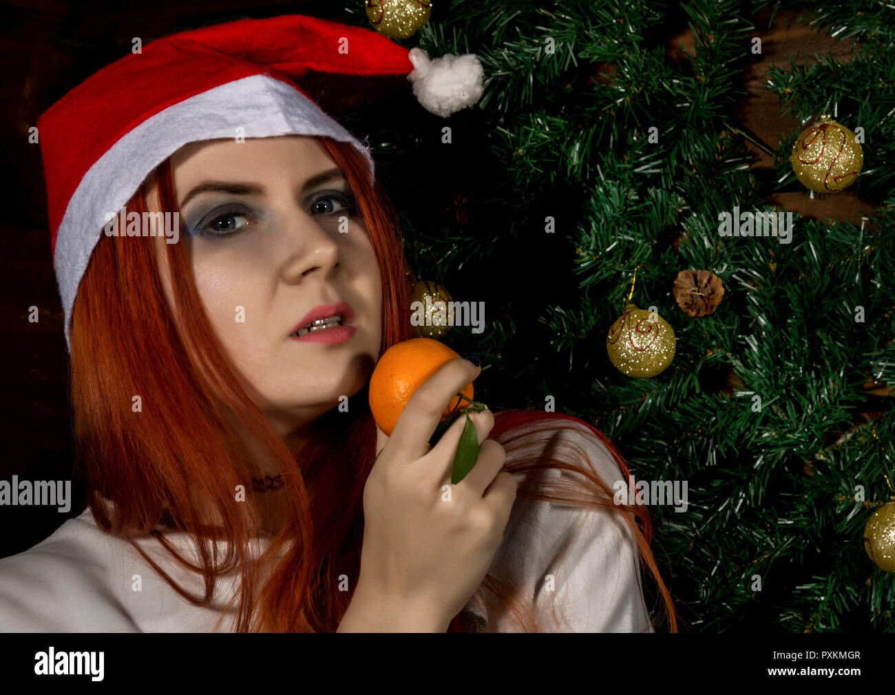 Beautiful redhead woman wear santa hat and eating tangerine. concepte of waiting Christmas and New Year Stock Photo