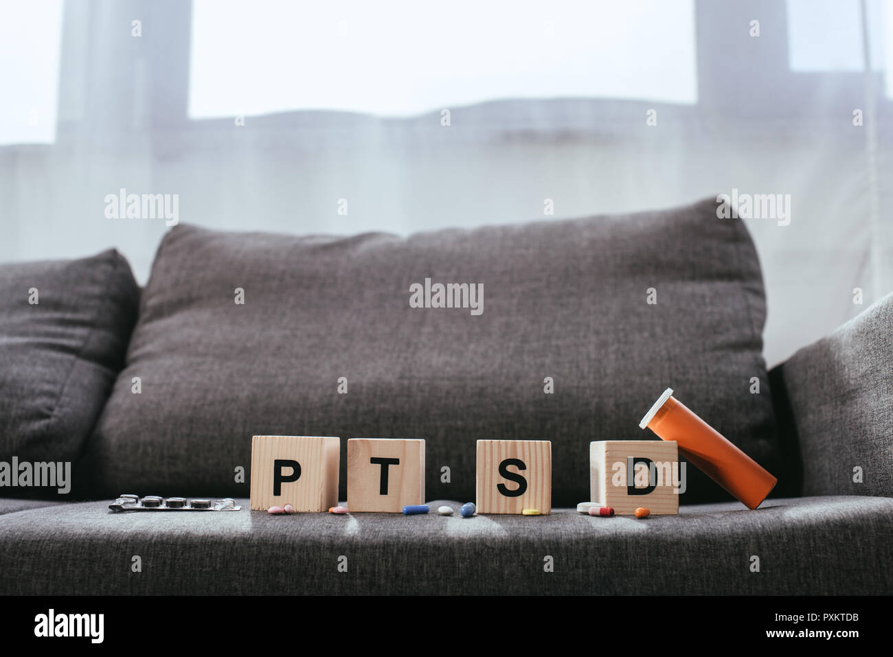 wooden cubes with posttraumatic stress disorder abbreviation signs (PTSD) lying on couch with various pills Stock Photo