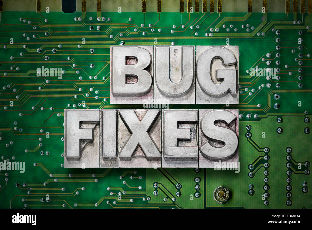 bug fixes phrase made from metallic letterpress blocks on green pc board background Stock Photo