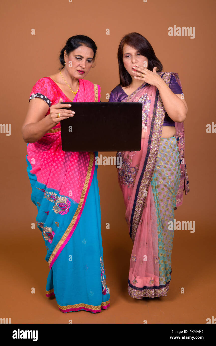 Two mature Indian women using laptop computer and looking shocked and surprised Stock Photo