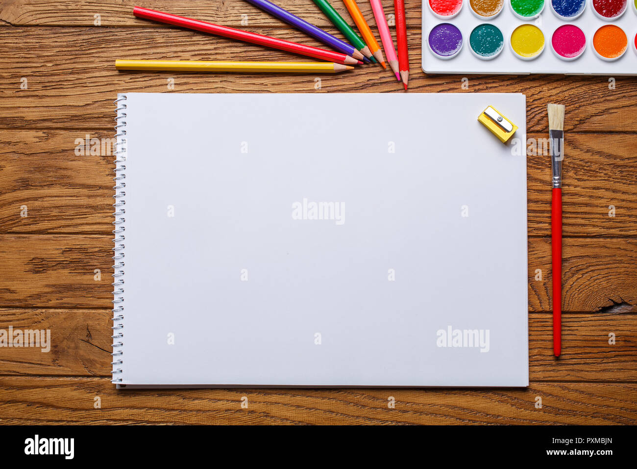 On the wooden table there is an album for painting, paint, pencils and brushe. On a wooden background. Top view, flat lay. copyspace Stock Photo