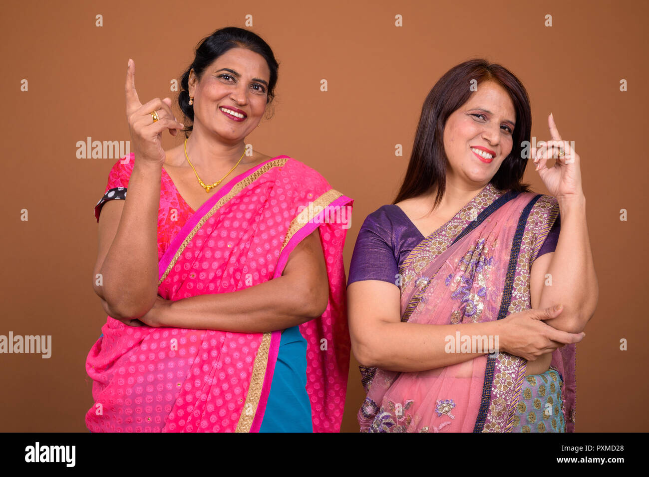 Portrait of two happy Indian women pointing finger up together Stock Photo