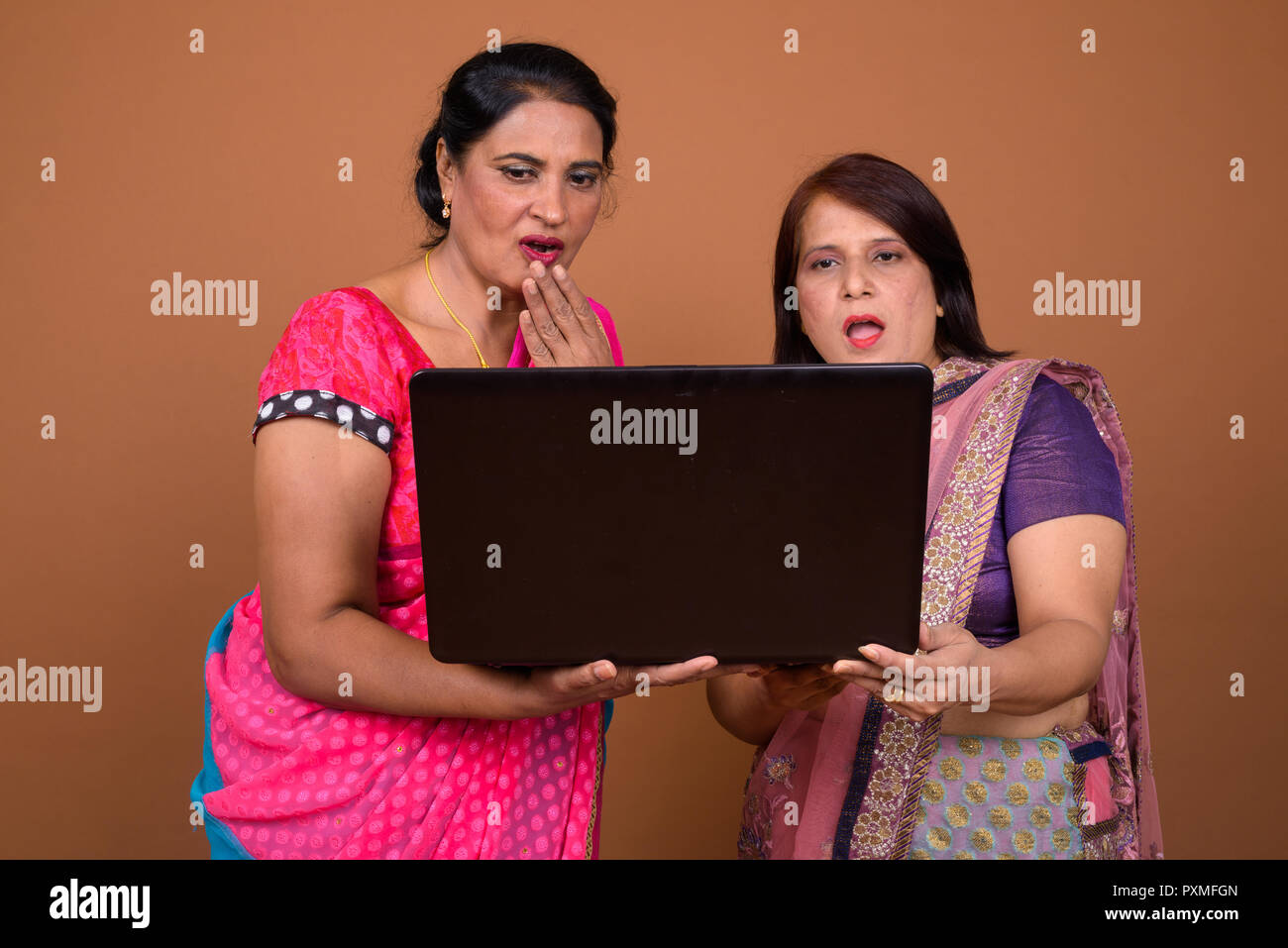Two happy Indian woman using laptop computer and looking shocked and surprised Stock Photo