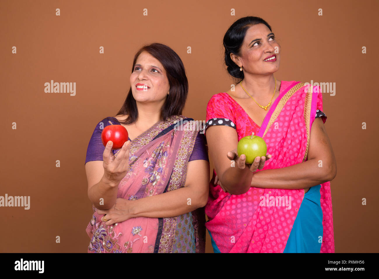 Two happy Indian woman holding apple while thinking Stock Photo