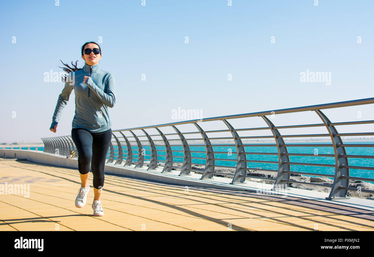 Girl running on the boardwalk for a workout by the sea Stock Photo