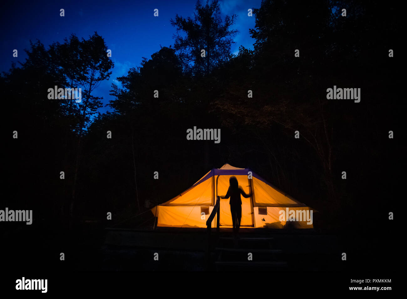 Silhouette of person in front of illuminated tent at night in eco resort in Slovenia. Stock Photo