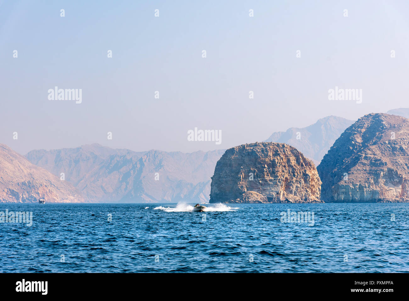 Boat floating on seaside surrounded by desert rocks near Khasab, Musandam Oman Stock Photo