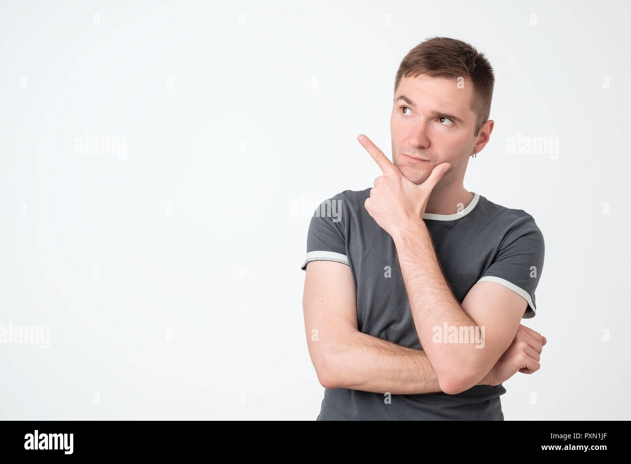 Handsome pensive guy with good-looking hairstyle looking aside and pointing with index finger. Copy space. Stock Photo