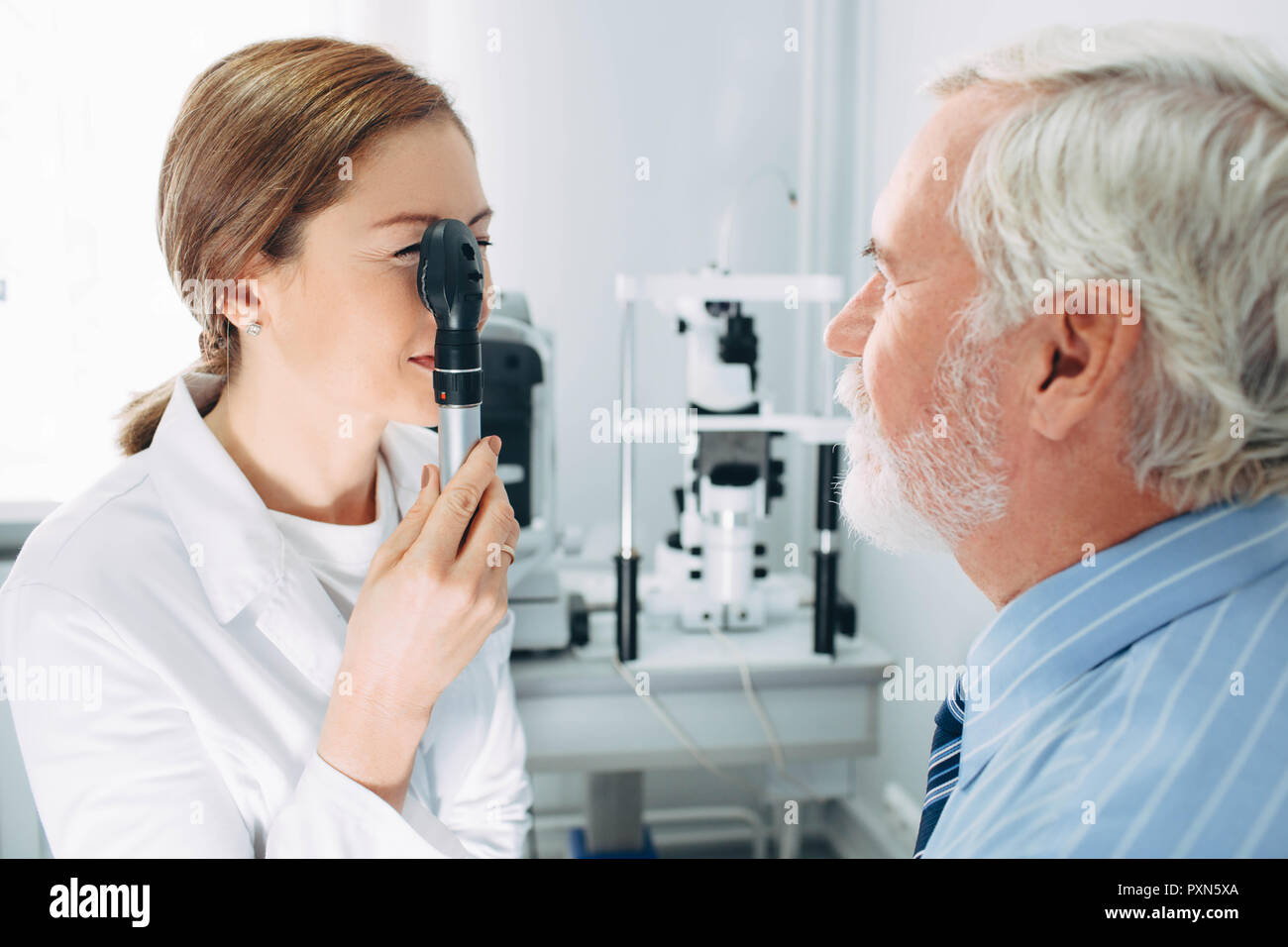 Doctor Optometrist examining old man's eyes with ophthalmoscope. Eye