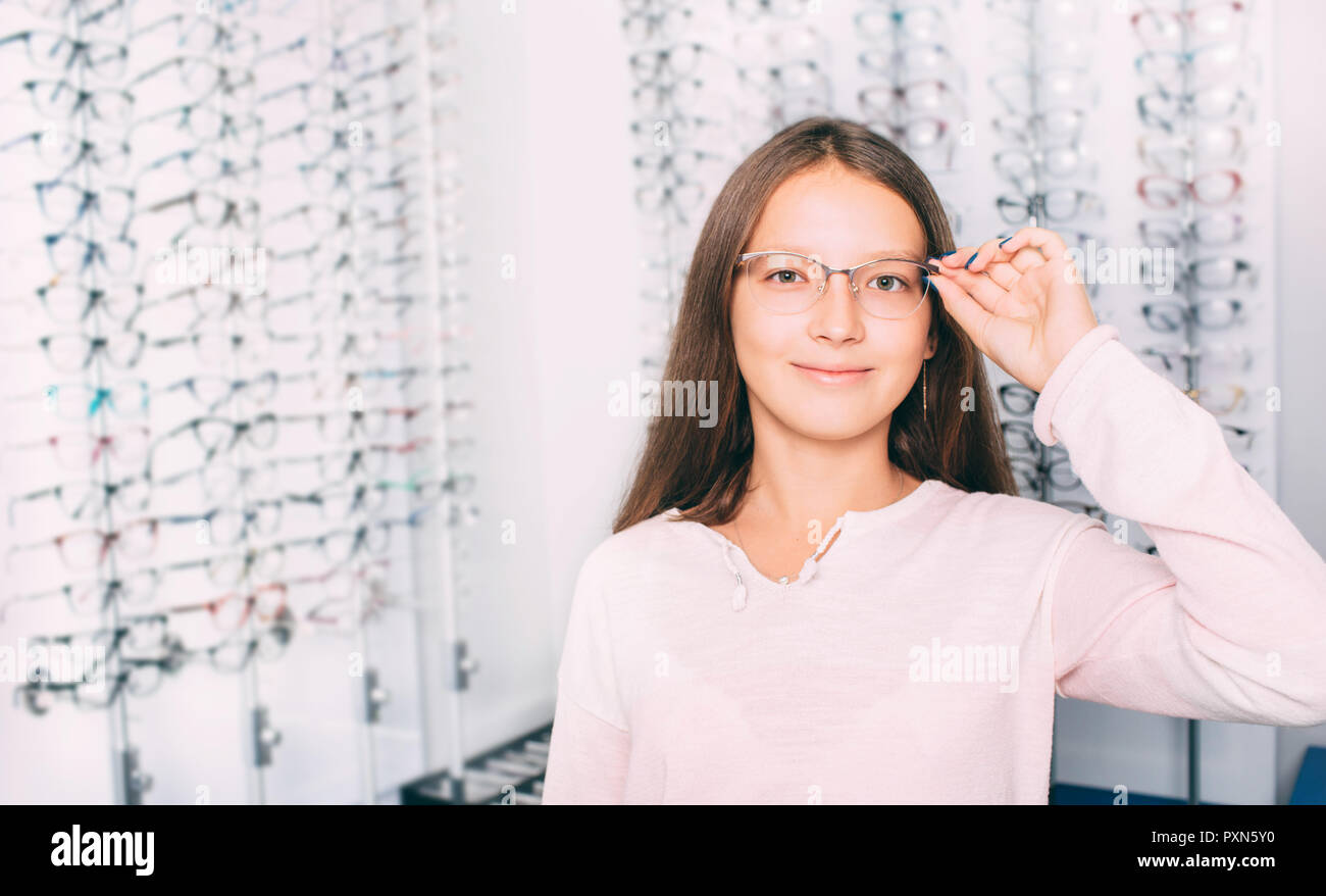 teenage girl adjusting her new eyeglasses while standing at optics store Stock Photo
