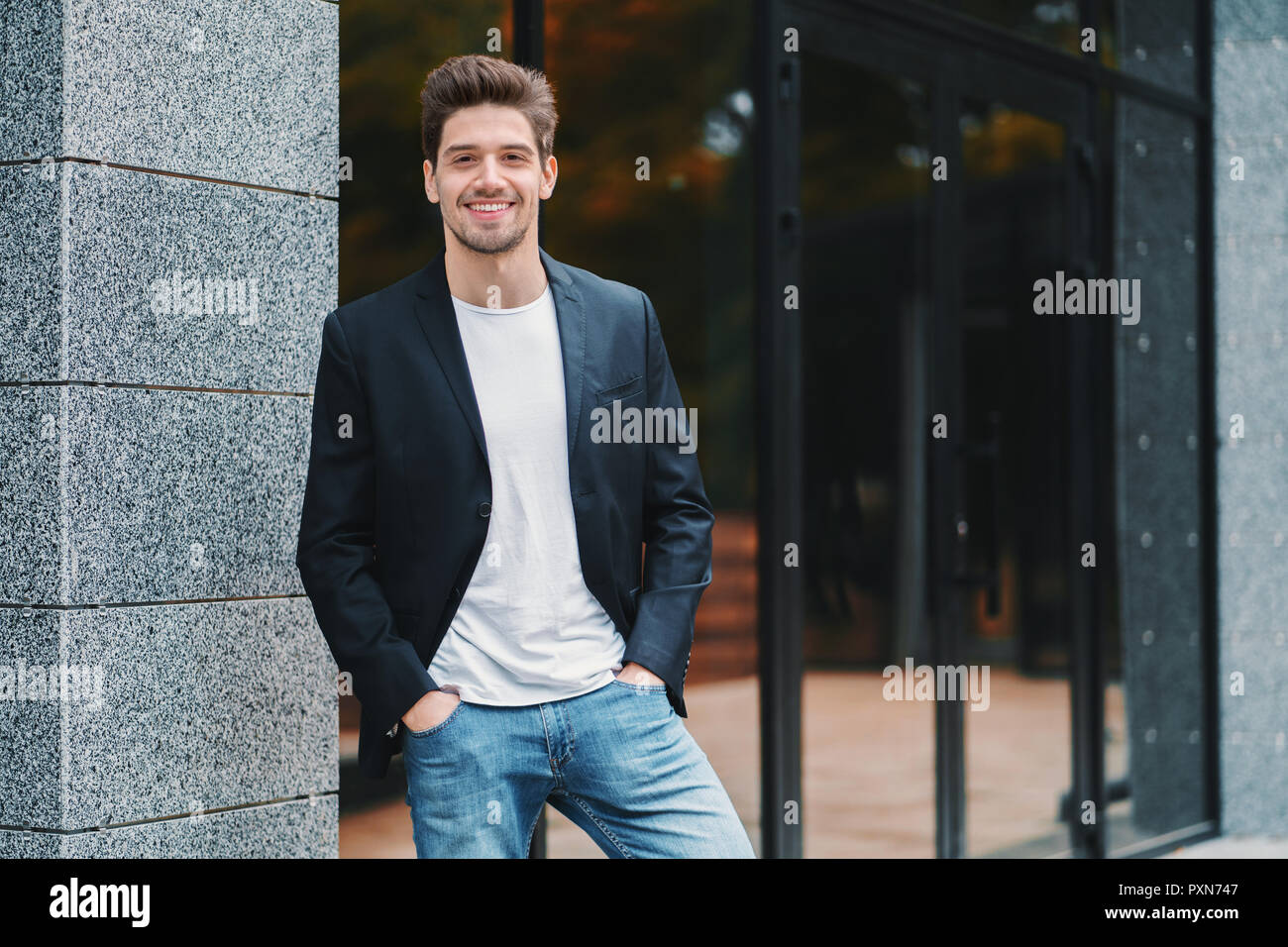Portrait of young successful confident businessman in the city on office building background. Man in business suit looking to camera and smiling. Portraiture of handsome guy Stock Photo