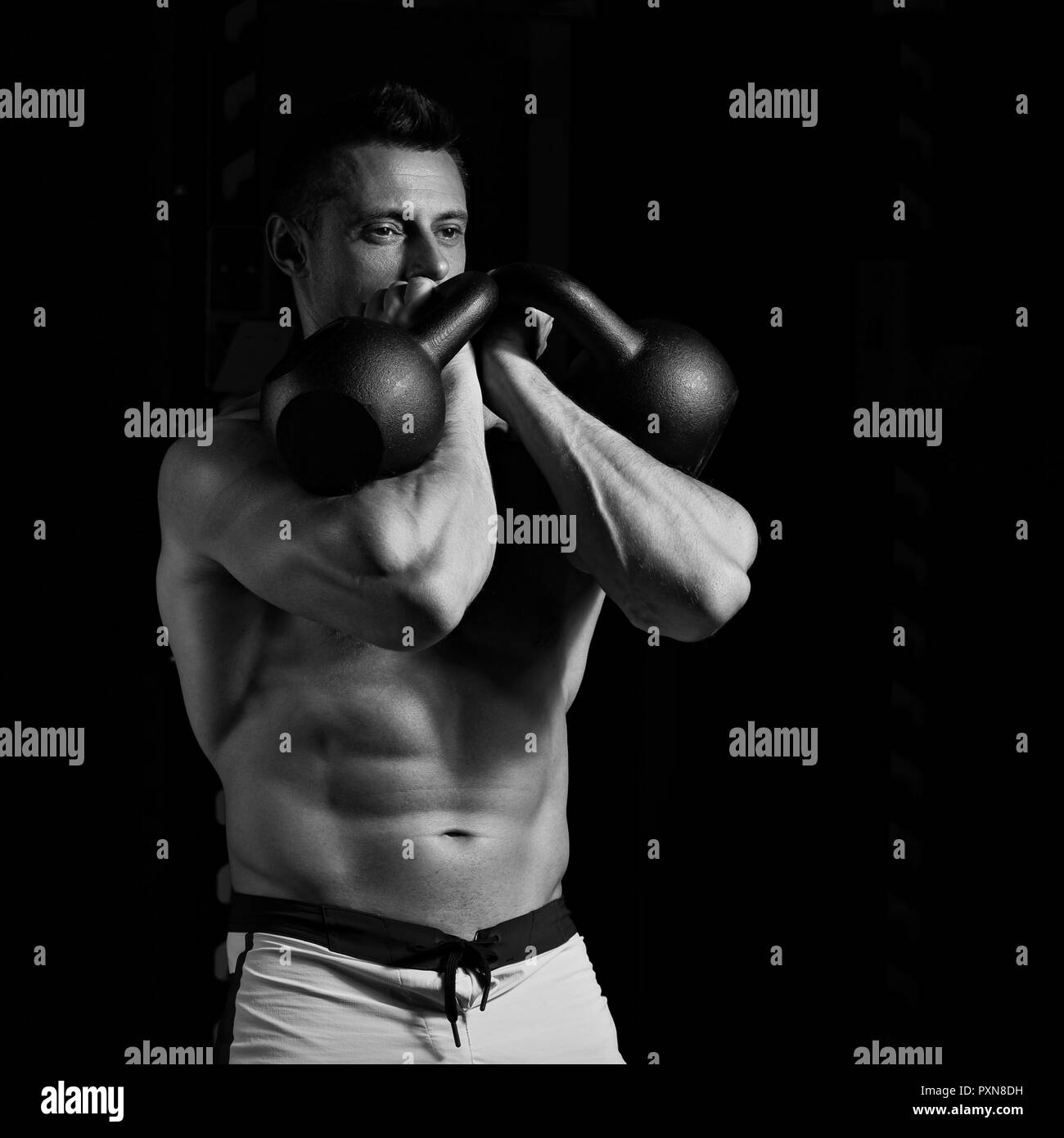 Handsome strong man doing the exercises with kettlebells on dark shadow background. Closeup contrast portrait. Black and white Stock Photo