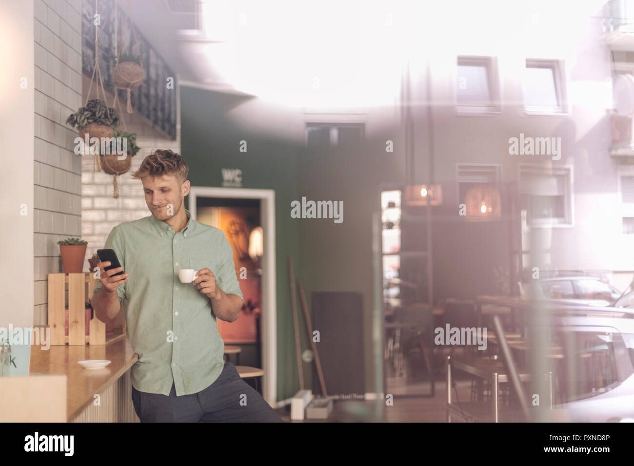 Young business owner drinking coffee, checking smartphone Stock Photo