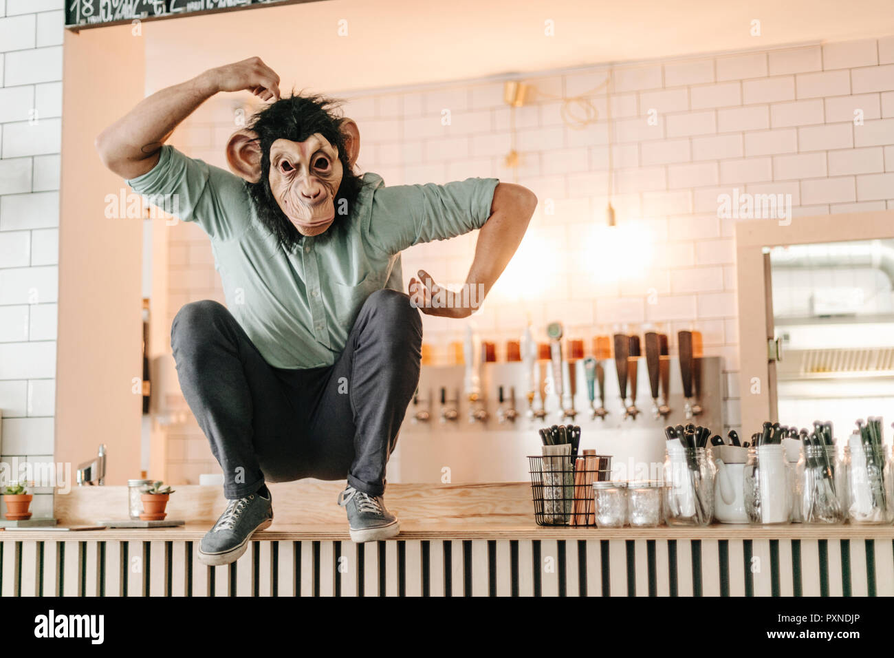 Man wearing monkey mask, sitting on counter of a bar, scratching head Stock Photo