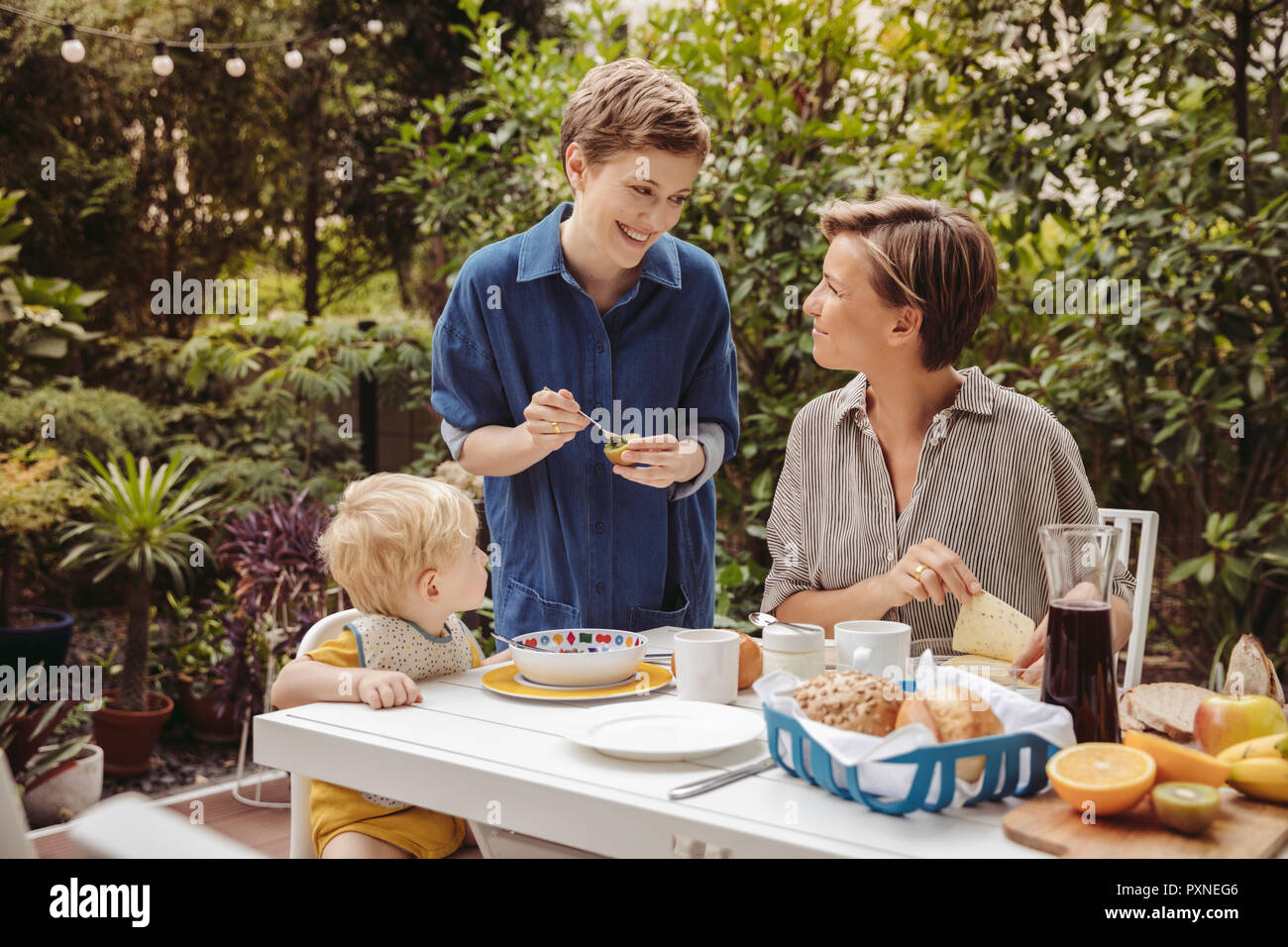 Two happy mothers at breakfast table outdoors with their child Stock Photo