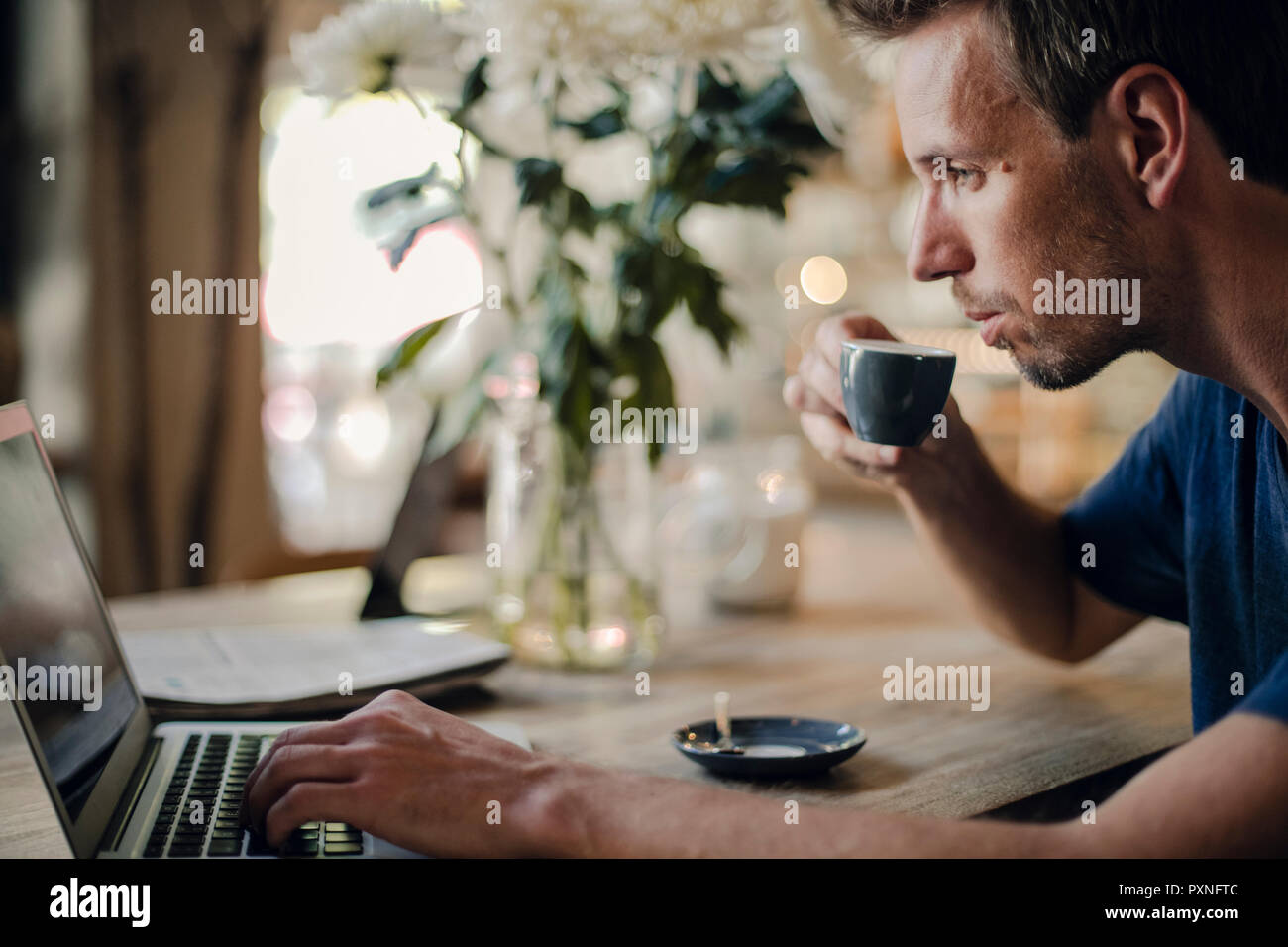 Mid adult man sitting in coffee shop, drinking coffee, using laptop Stock Photo