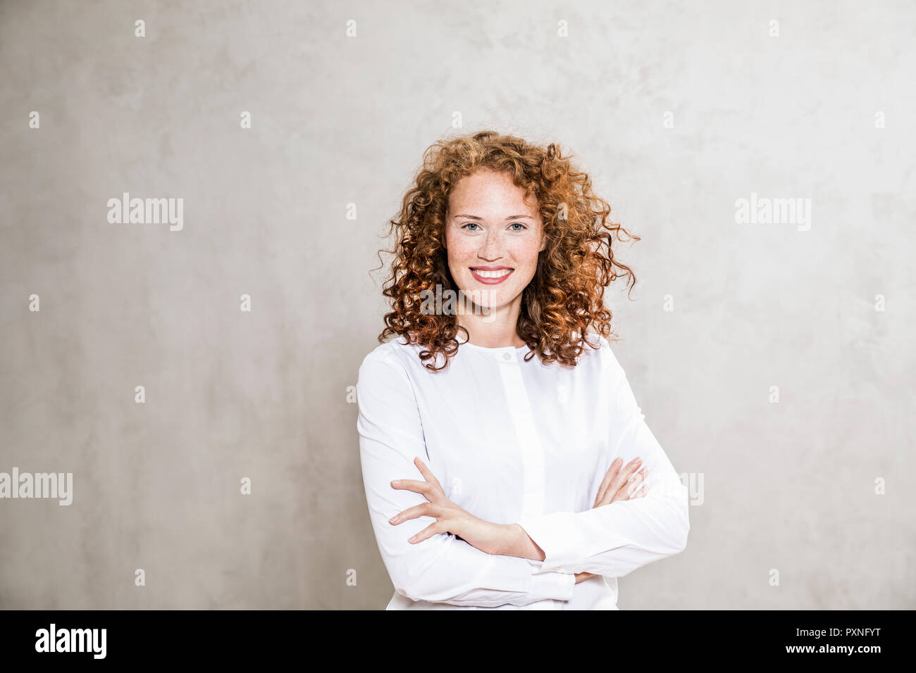 Portrait of laughing redheaded young woman with arms crossed Stock Photo