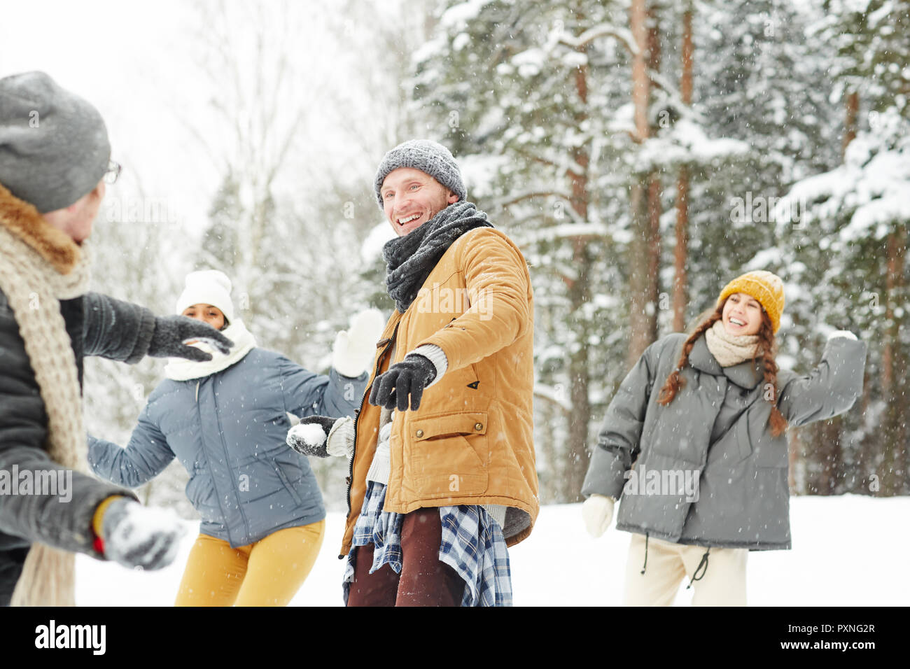 Carefree friends enjoying snowball fight: cheerful excited young man throwing snowball and looking at friend in winter park Stock Photo