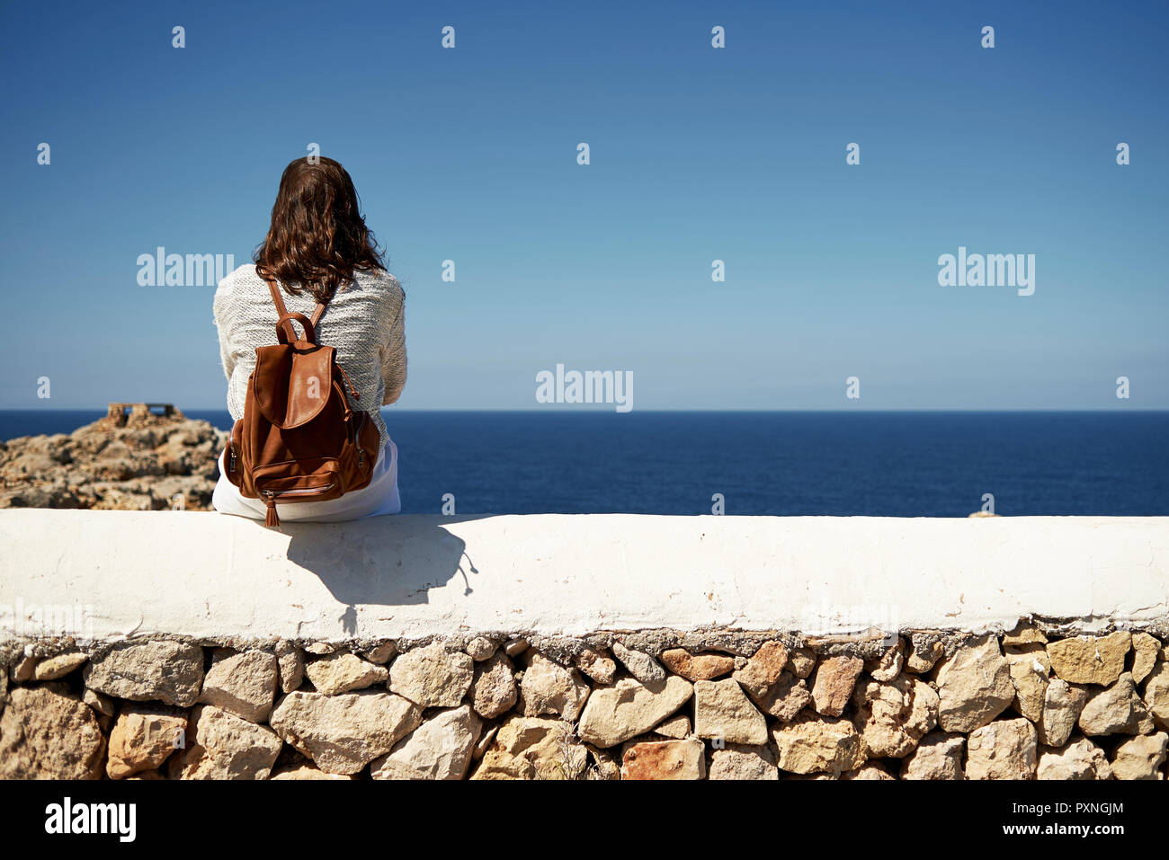 Young brunette woman sitting on wall, looking at view Stock Photo