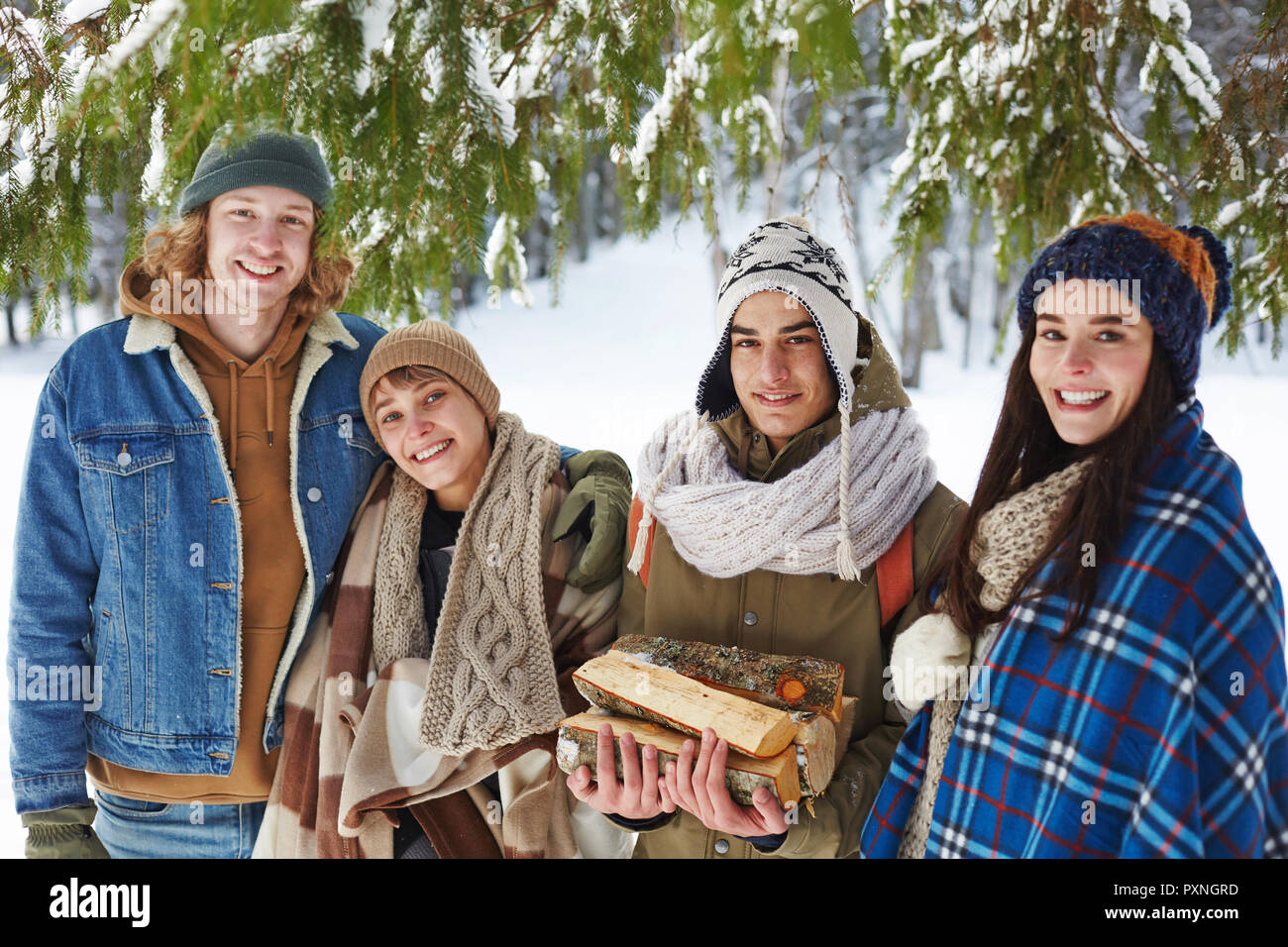 Portrait of two beautiful young couples posing in snowy winter forest standing under fir tree and smiling at camera, copy space Stock Photo