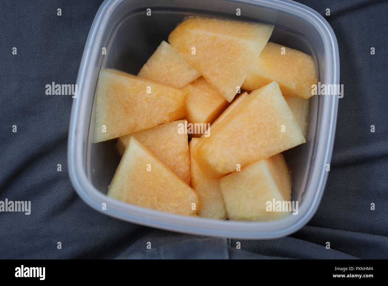 Melon Pieces. Fresh peeled pieces of melon in a plastic box on the knees, close up. Healthy snack on the way. Stock Photo