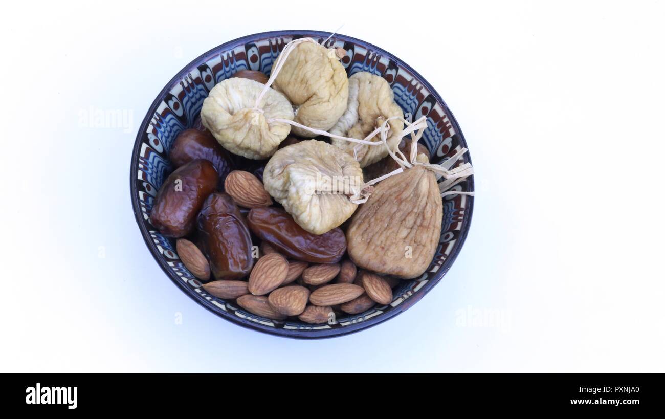 Dried Fruits in an Oriental Bowl. Decorated dish with dried fruit: Figs, dates and natural almonds, Top view, close up, isolated on white background. Stock Photo