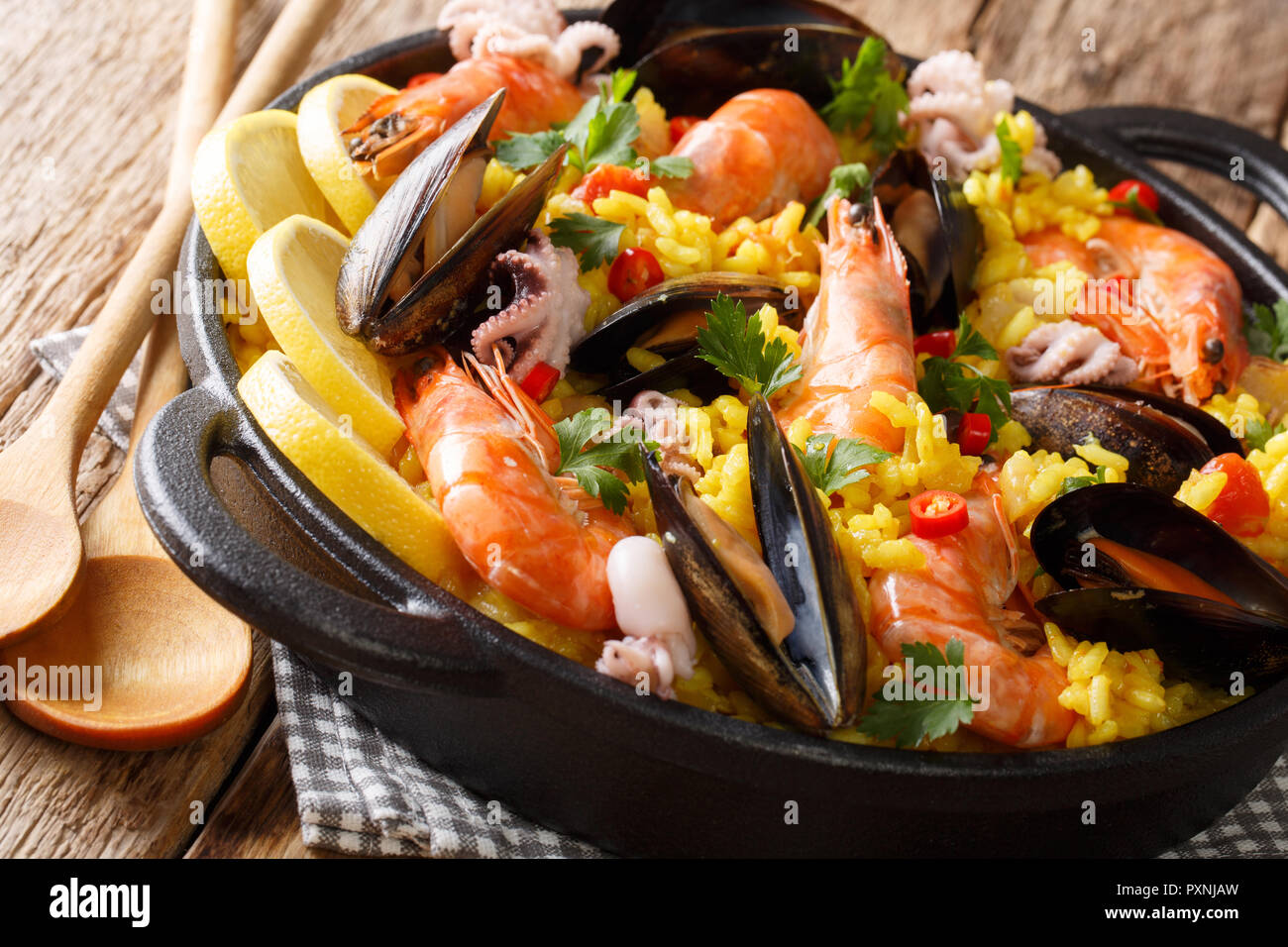 Spanish traditional cuisine: hot paella with seafood shrimps, mussels, fish, and baby octopuses close-up in a frying pan on the table. horizontal Stock Photo