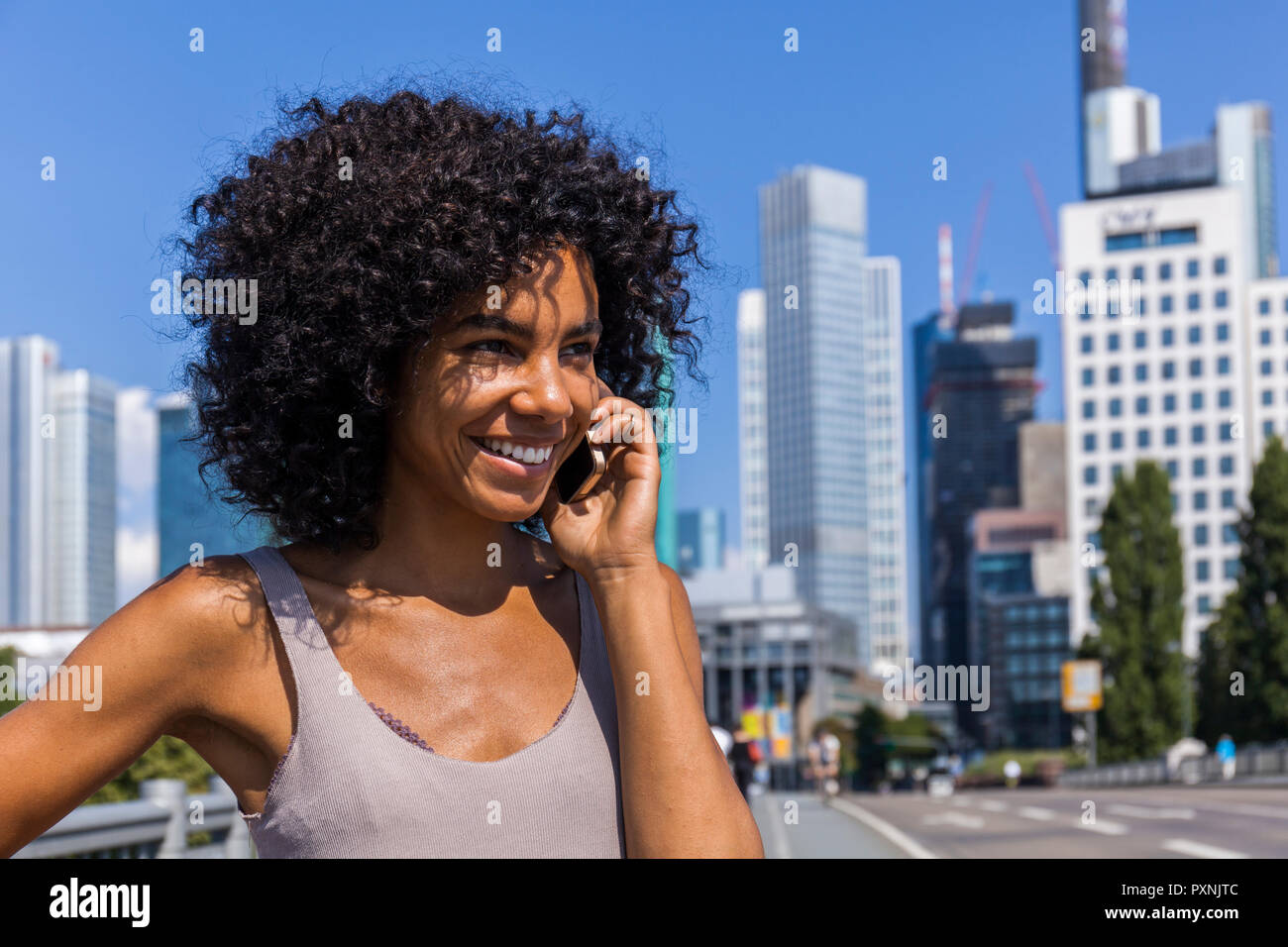 Germany, Frankfurt, portrait of smiling young woman with curly hair on the phone Stock Photo