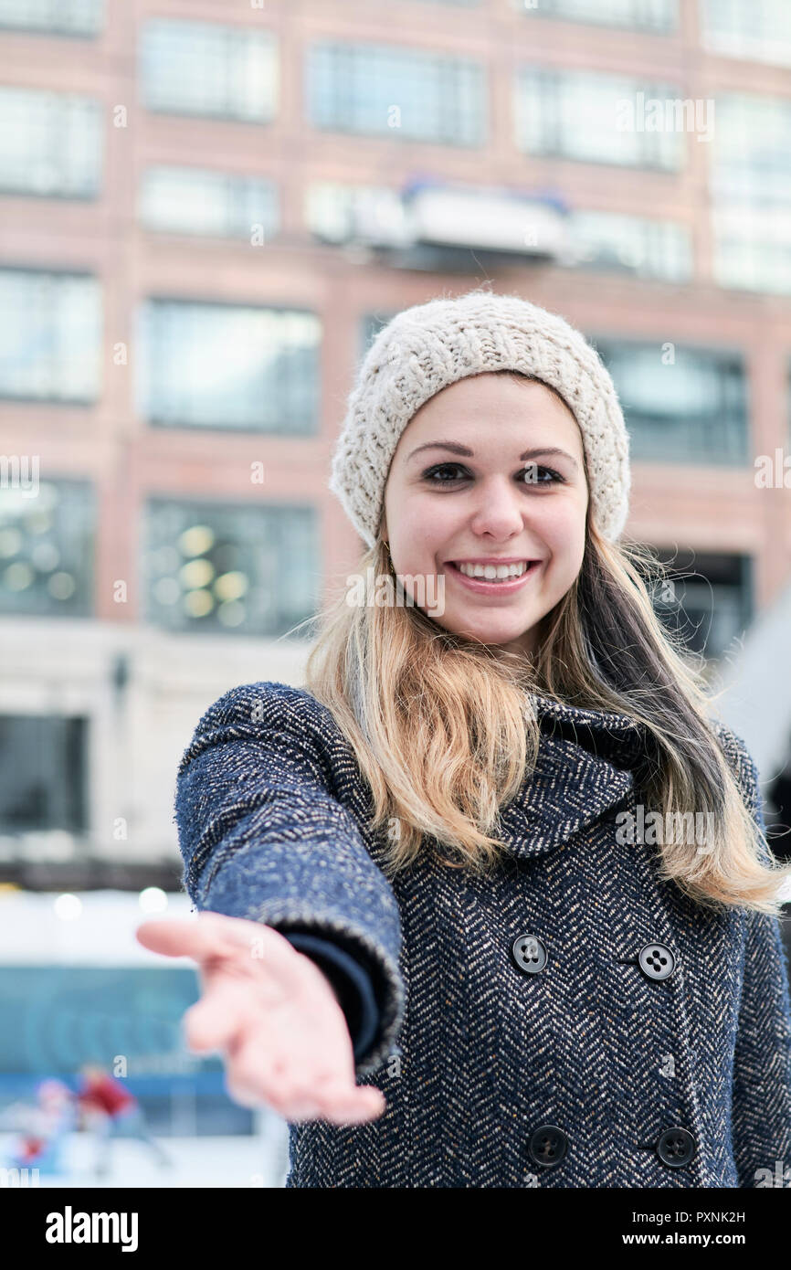 Pretty blond young woman wearing wool cap in winter, reaching out hand Stock Photo