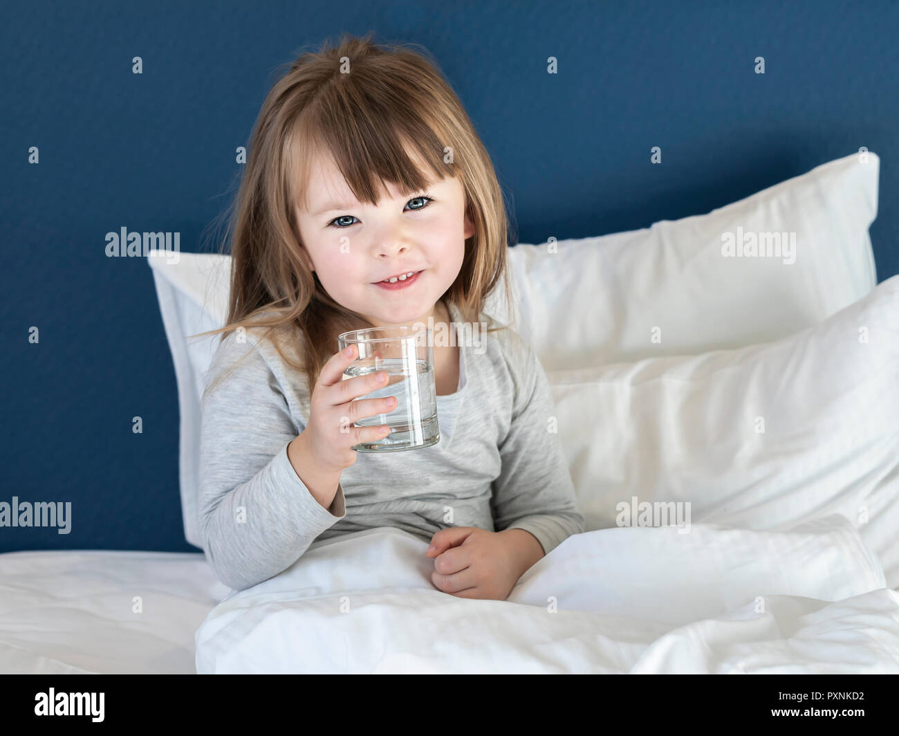 Beautiful little girl drinking water on white bed Stock Photo Alamy