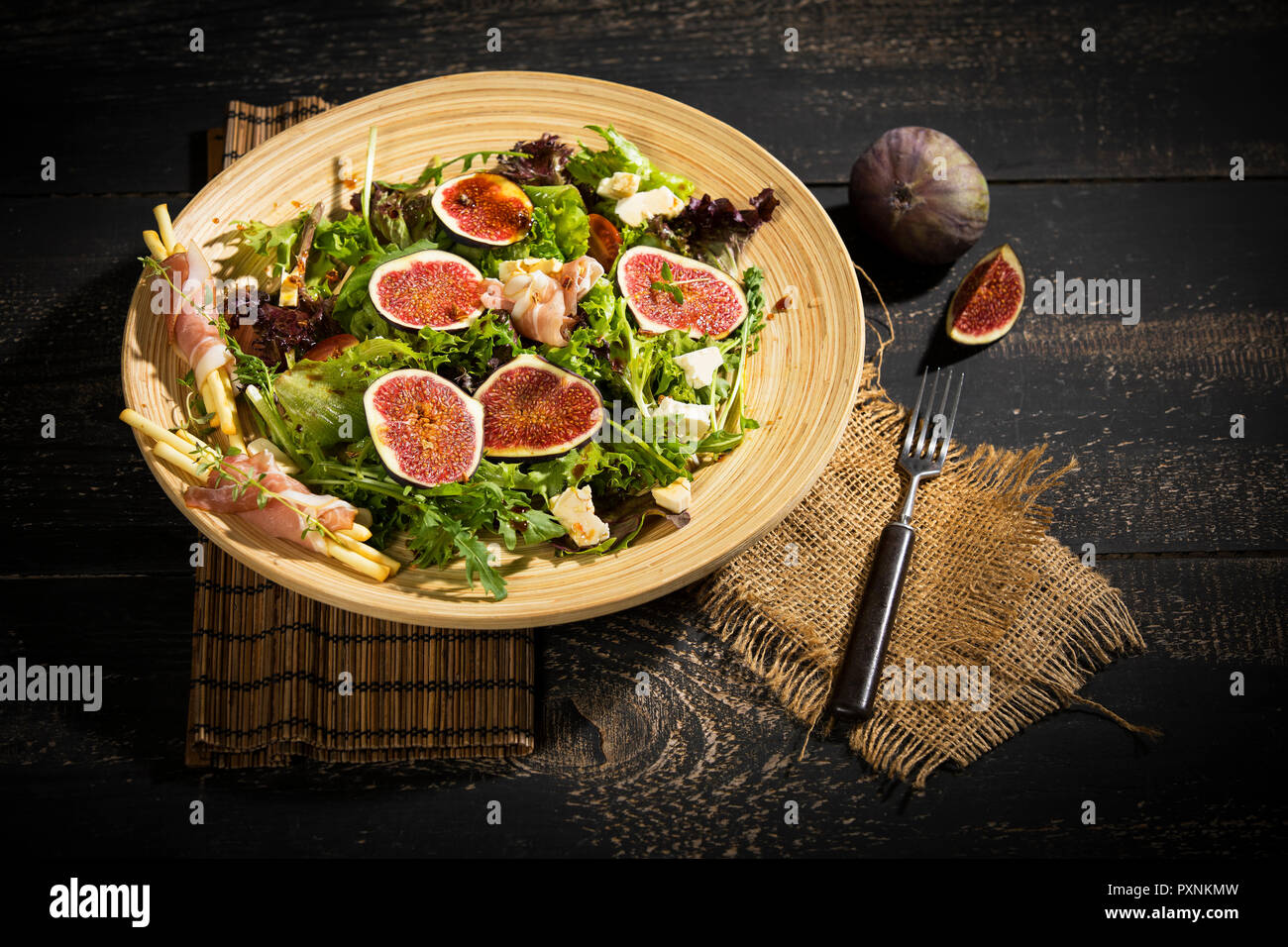 Mixed salad with figs, tomatoes, sheep cheese, grissini with ham on bambus plate Stock Photo