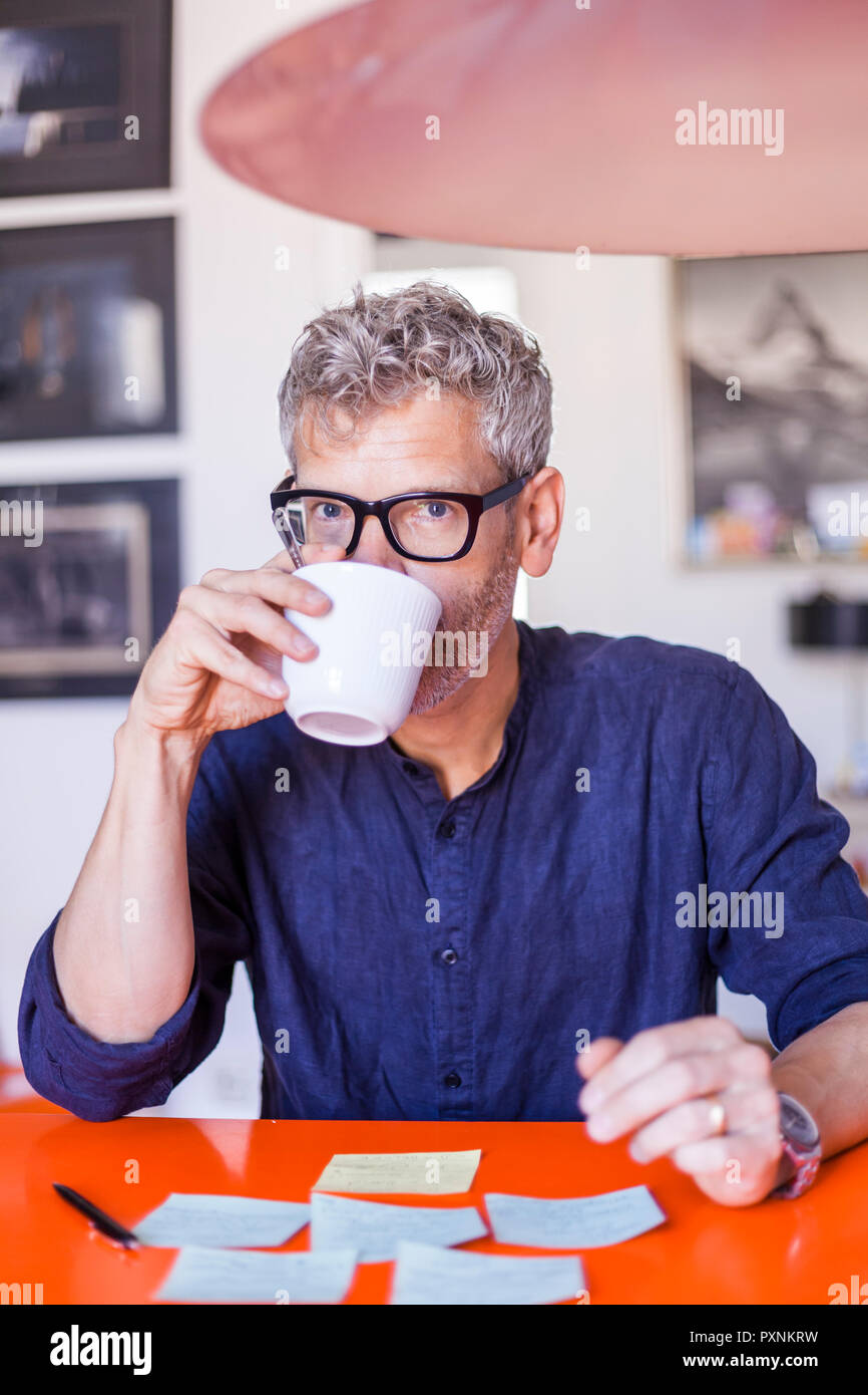 Portrait of mature man at table with notepads drinking coffee Stock Photo